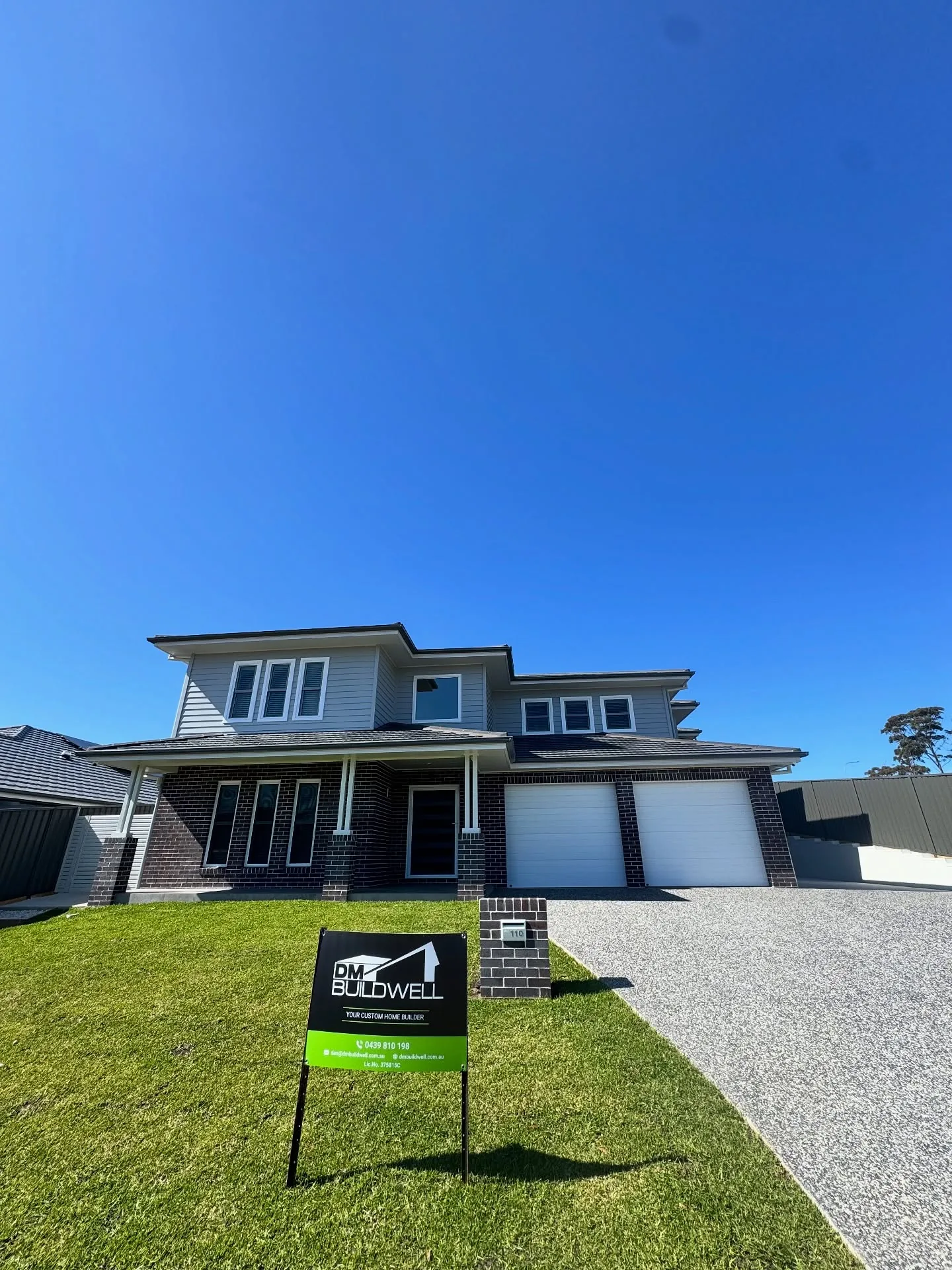 Two-storey new-build home with dark brick base and pale weatherboard cladding