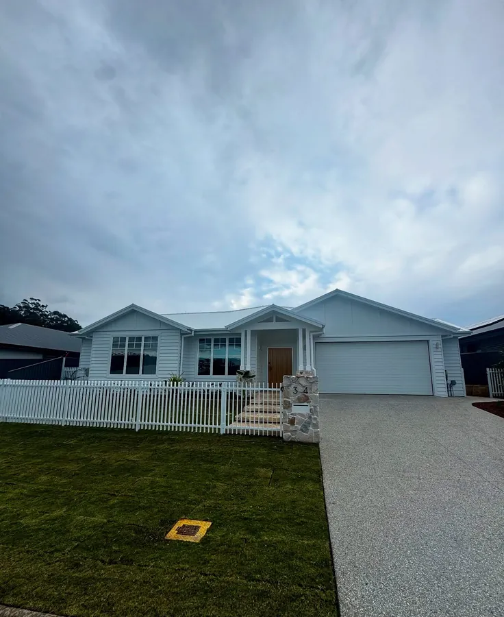 Single-storey Hamptons-style weatherboard home behind a white picket fence